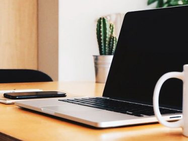 Laptop, coffee mug and mobile phone sitting on a wooden desk