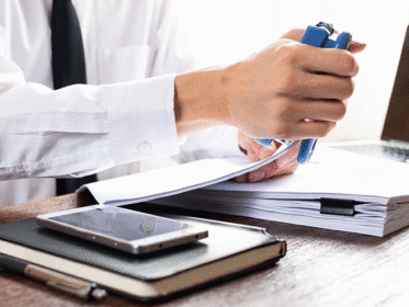 Caucasian man dressed in white shirt and dark tie sitting at a desk and stapling documents together