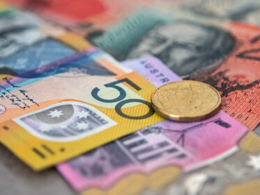This image is a close-up shot of five, twenty and fifty dollar Australian notes on a grey surface. On top on the notes is an Australian two dollar gold coin.